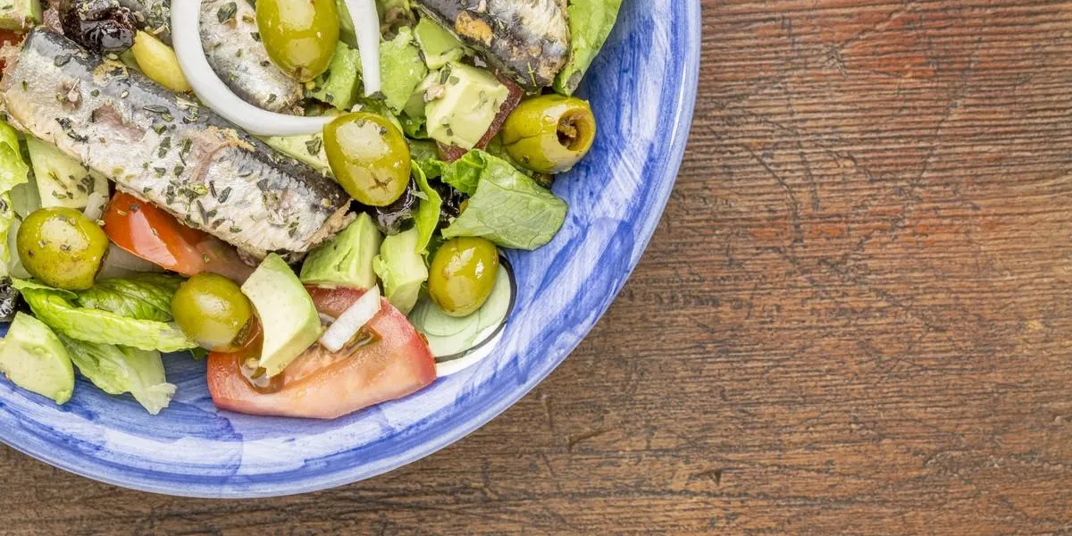 sardine salad (canned sardines, romaine lettuce, tomato, avocado, onion, olives) in bowl against grunge wood