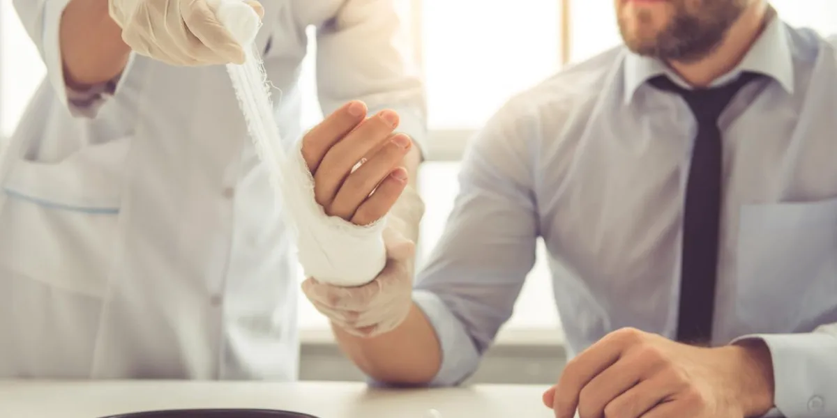 cropped image of female doctor bandaging man's injured hand while working in her office