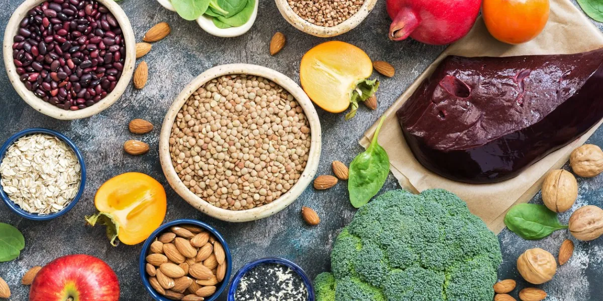 foods high in iron liver, broccoli, persimmon, apples, nuts, legumes, spinach, pomegranate top view, flat lay