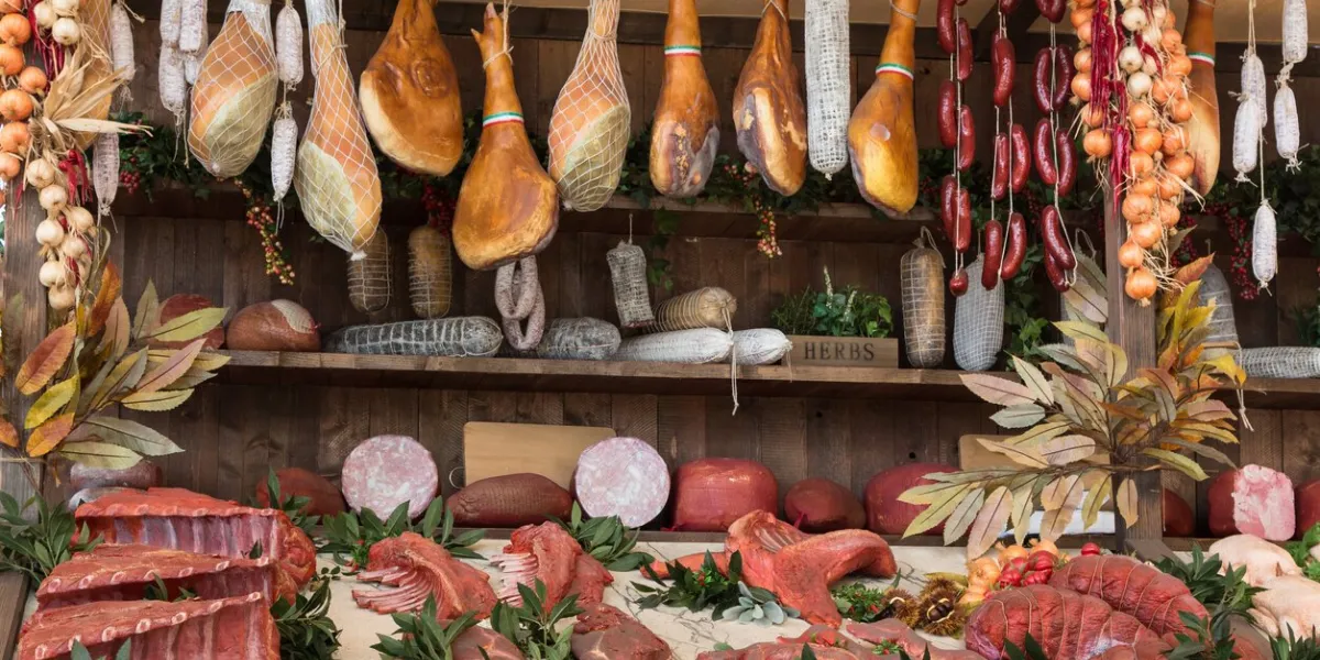 variety of raw meat and sausages in butcher shop on wooden board
