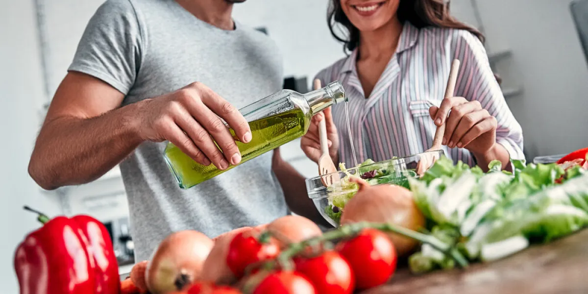 romantic couple is cooking on kitchen handsome man with a bottle of oil and attractive young woman are having fun together while making salad healthy lifestyle concept