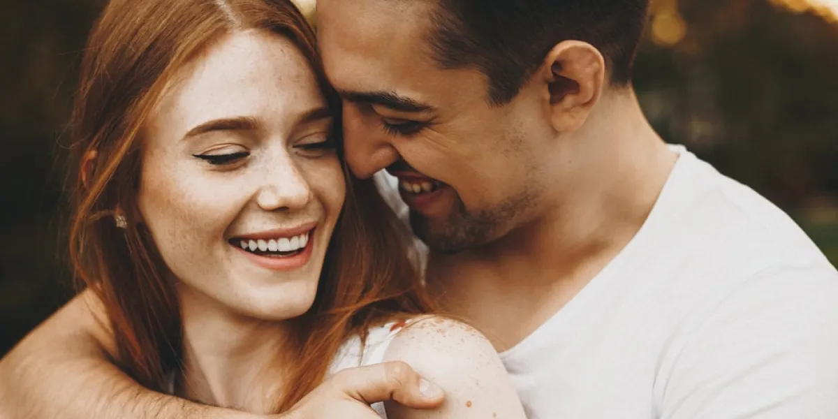 close up portrait of a charming young couple laughing while man is embracing her girlfriend against sunset outdoor in park