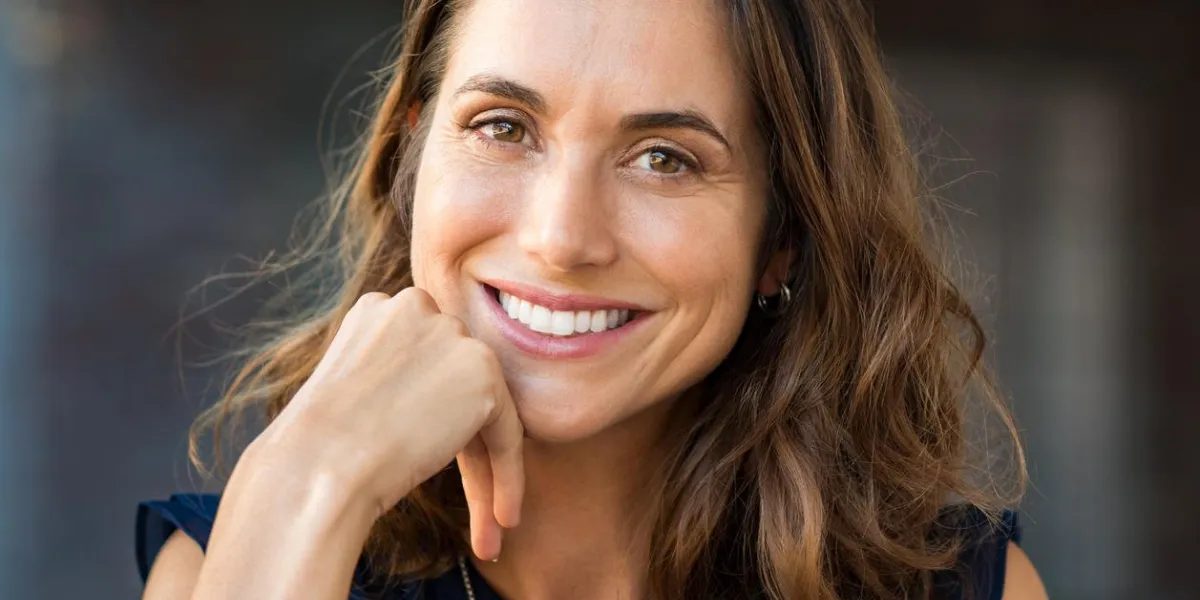 portrait of a happy smiling mature woman with hand on chin looking at camera close up face of beautiful latin woman with brown hair outdoor cheerful hispanic woman closeup