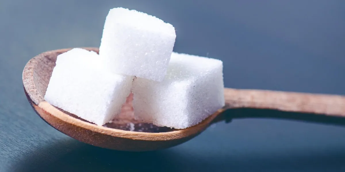 cubes de sucre sur une cuillère en bois fond bleu foncé aliments malsains