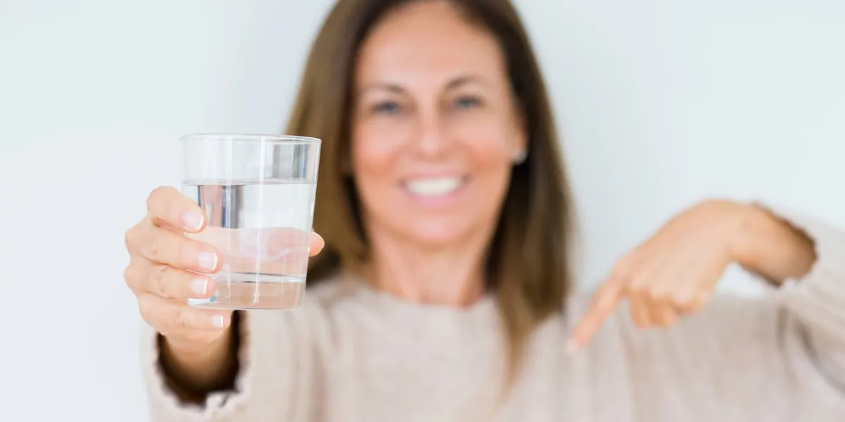 middle age woman drinking glass of water isolated background with surprise face pointing finger to himself