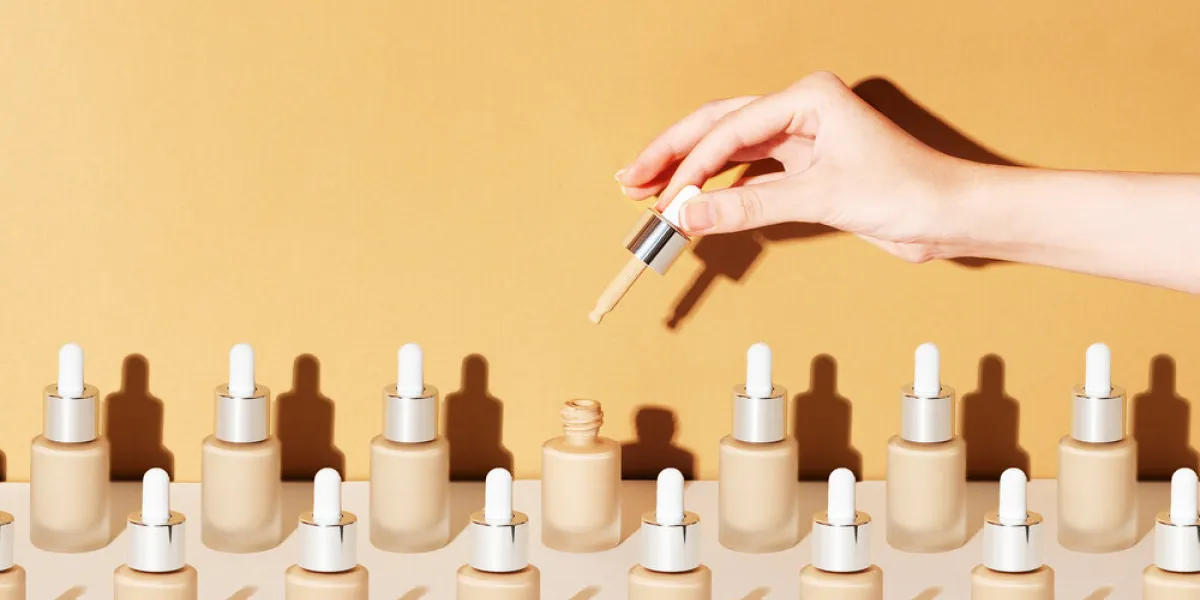 a female hand holds a dropper for applying bb foundation cream opened and closed jars of a cosmetic makeup product on a beige background pattern of beauty products packaging