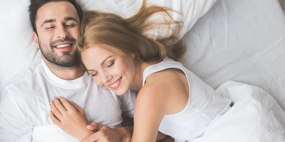 i am so happy with you top view portrait of cheerful young man and woman embracing while lying on bed they are smiling with closed eyes