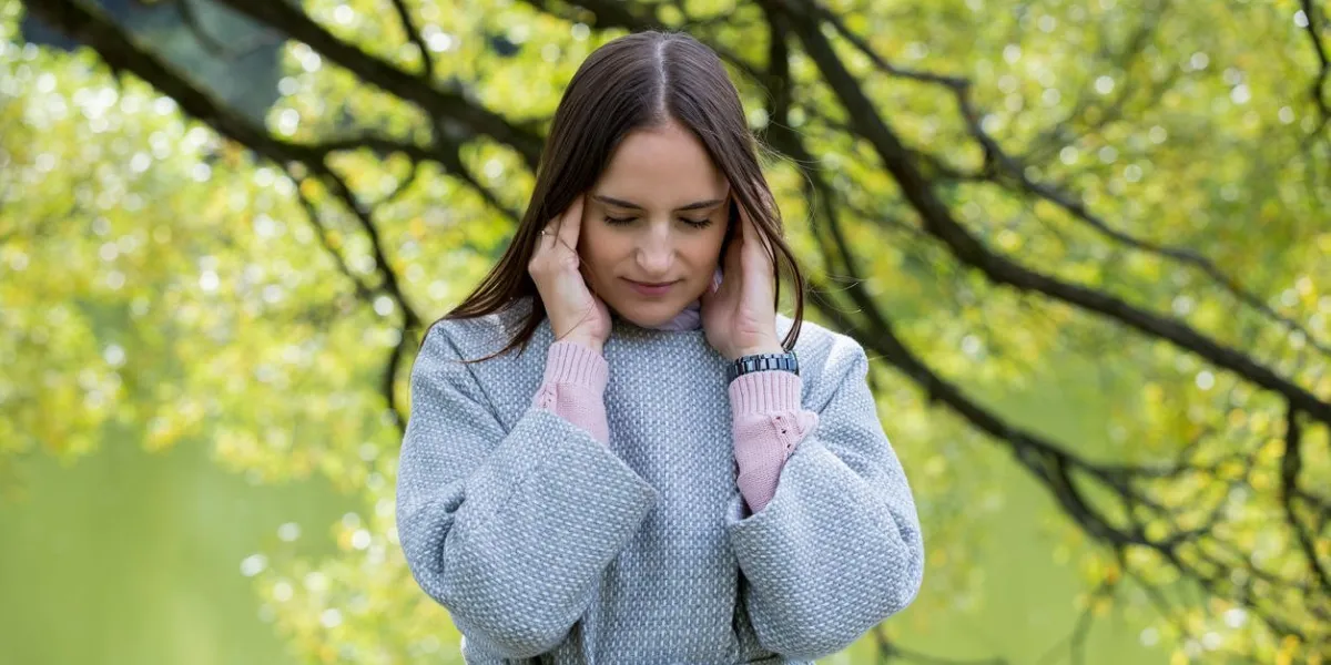 young beautiful woman standing in the park, suffering from headache touching temples, having pain looking stressful