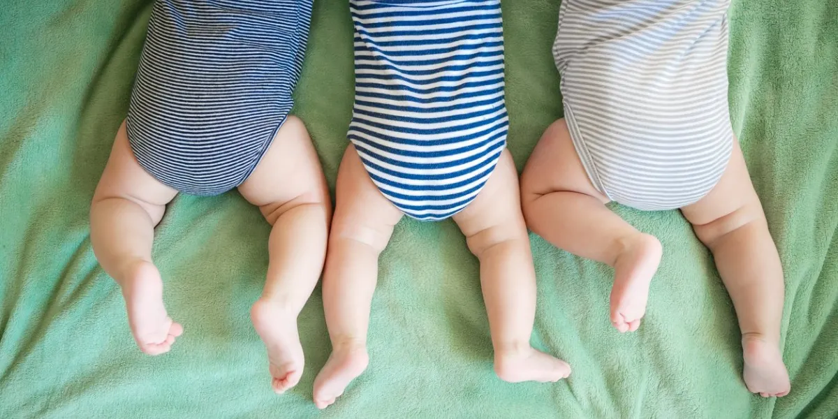 newborn triplets lie on a stomach on a blanket