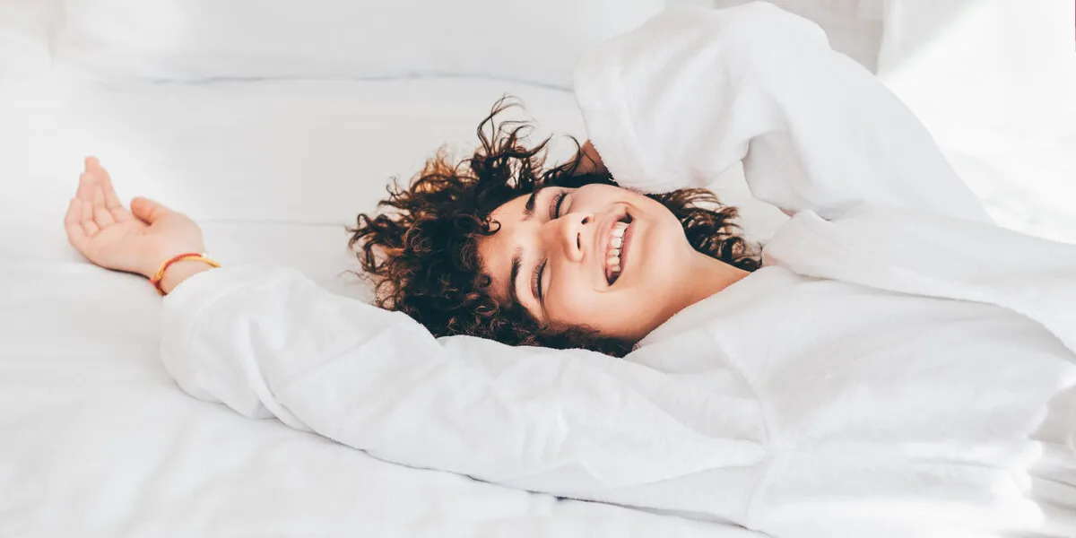 beautiful cheerful woman in a white bathrobe lying on the bed in the morning