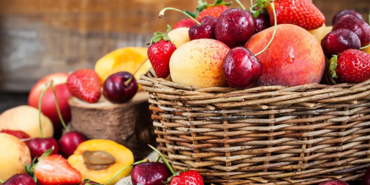 baies et fruits frais d'été mûrs (pêches, abricots, cerises et fraises) dans un panier en osier