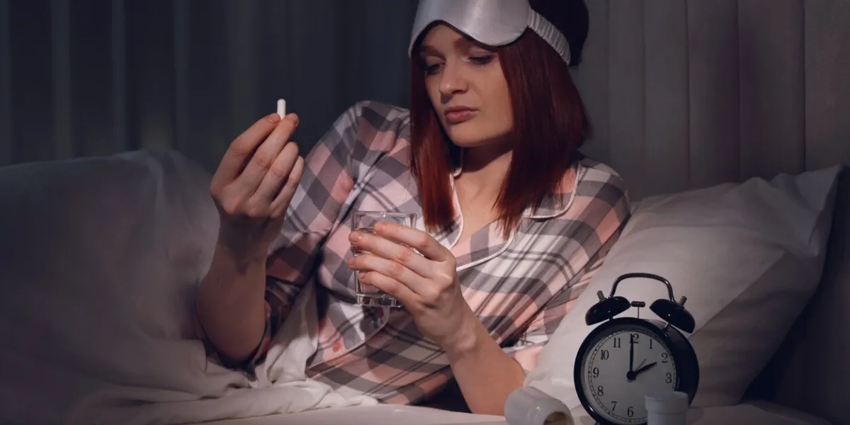 woman suffering from insomnia taking pill in bed at night