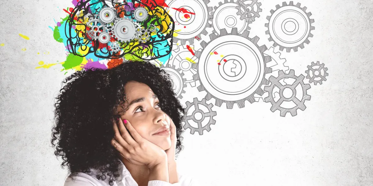 smiling young african american woman in white shirt looking at colorful brain sketch with gears drawn on concrete wall concept of brainstorming