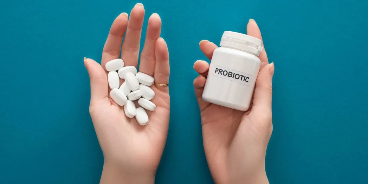 cropped view of woman holding white probiotic container and pills in hands on blue background