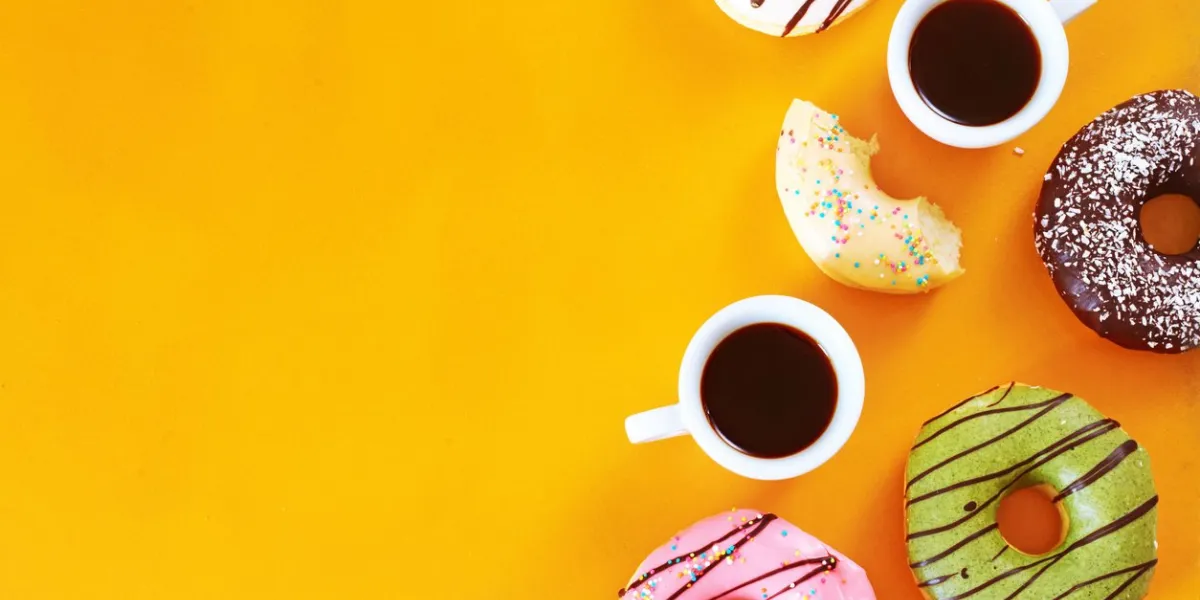 pistachio, chocolate, vanilla, strawberry donuts and two cups of espresso over yellow background