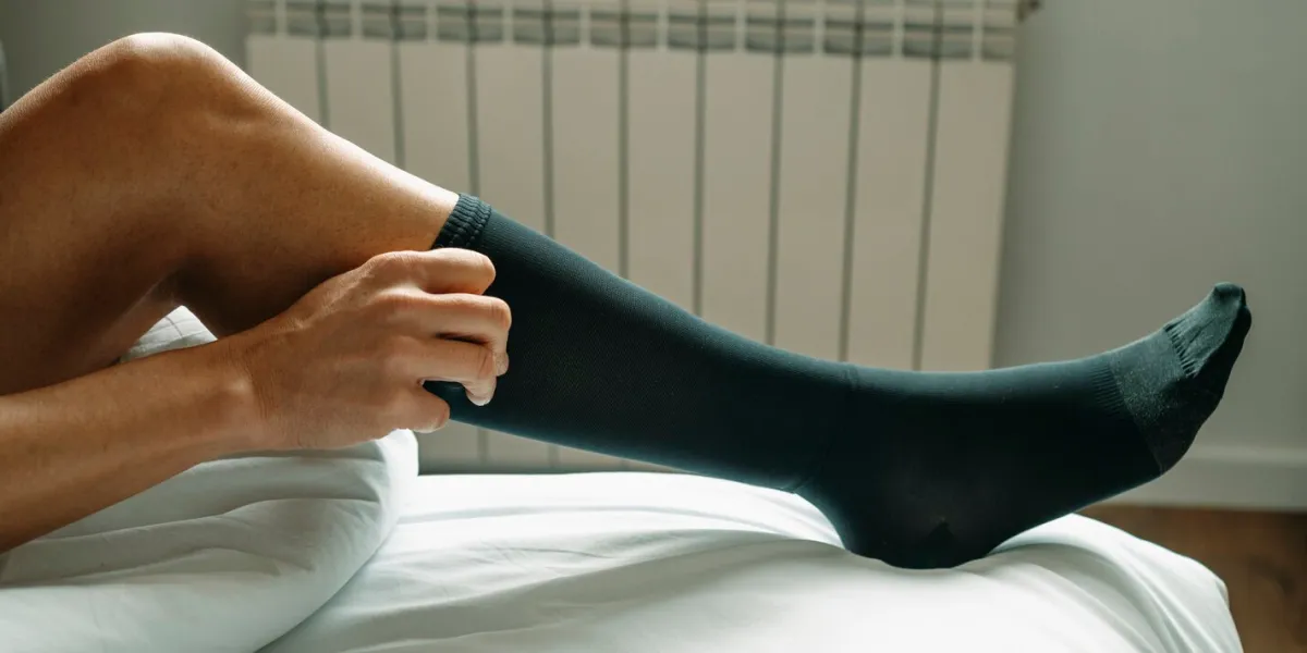 a man puts on a black compression sock sitting on his bed at home, in a panoramic format to use as web banner or header
