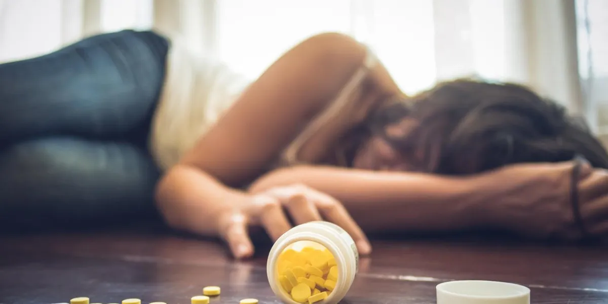 woman taking medicine overdose and lying on the wooden floor with open pills bottle concept of overdose and suicide