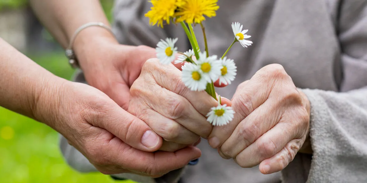 close up picture of elderly woman with dementia holding flower bouquet given by caretaker - hands