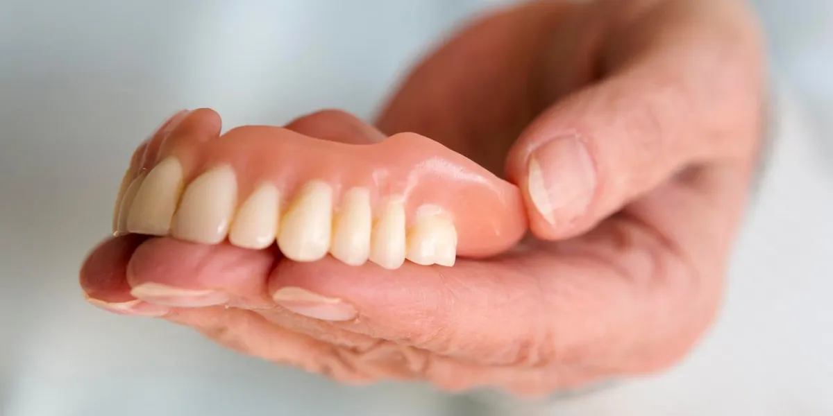 closeup of older womans hand holding a teeth denture