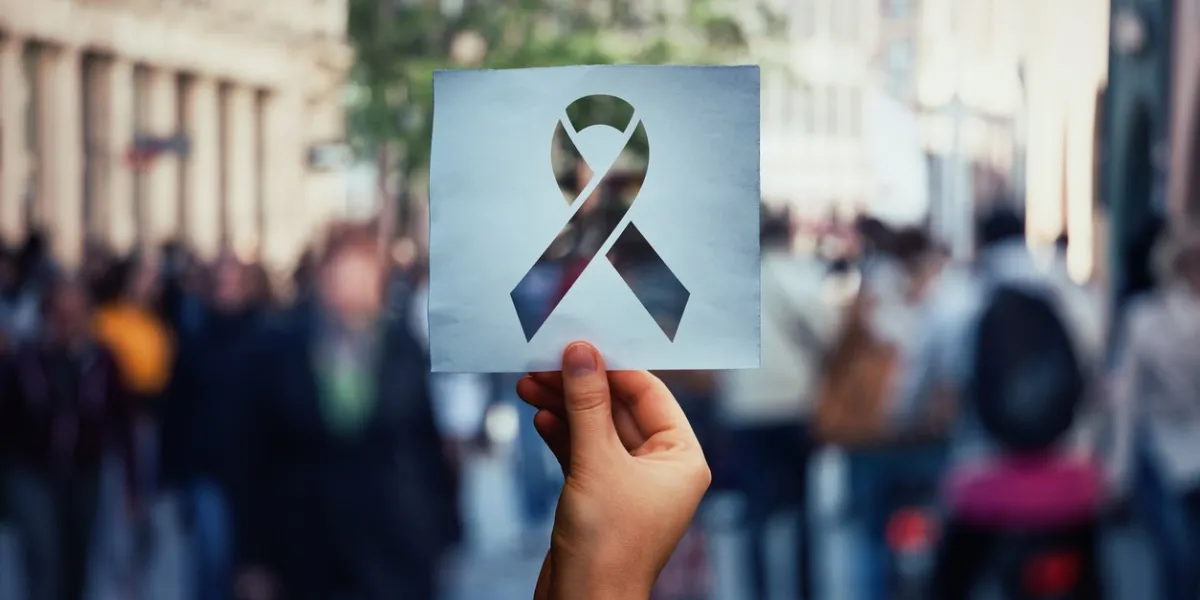 global issue stop aids as hand holding a paper sheet with hiv red ribbon symbol over crowded street background fight against cancer concept, substance abuse and anorexia awareness