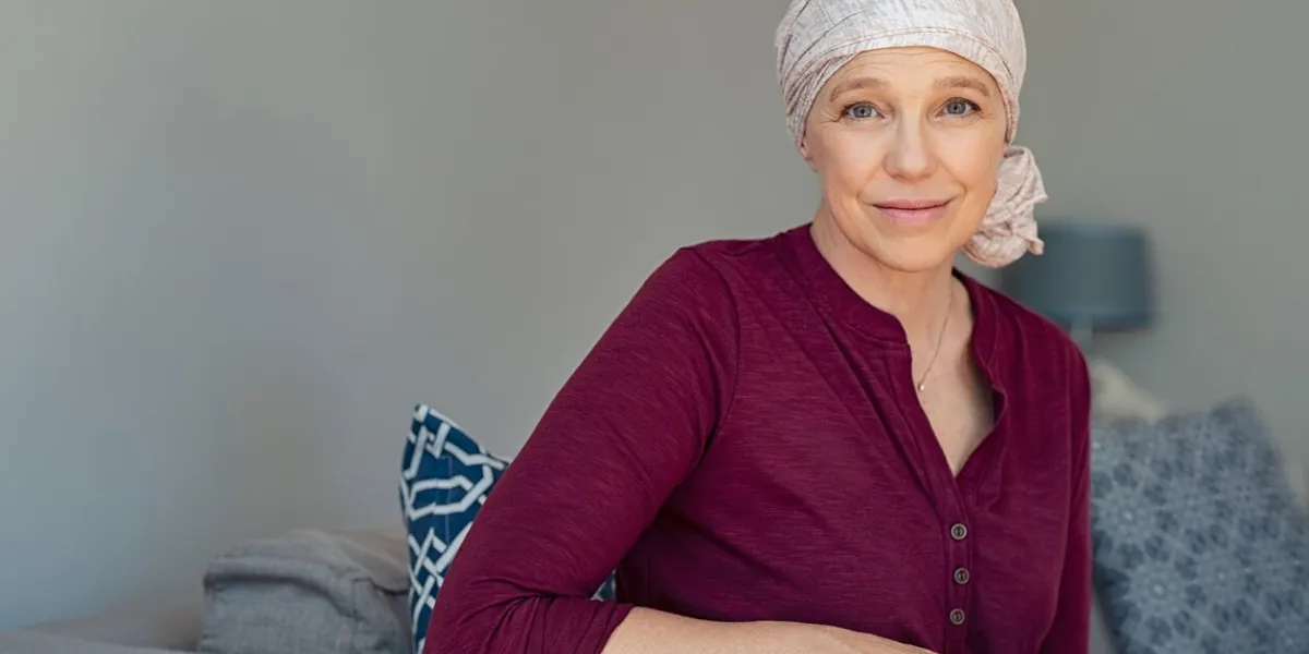 mature woman with cancer in pink headscarf smiling sitting on couch at home smiling woman suffering from cancer sitting after taking chemotherapy sessions portrait of mature lady facing side-effects of hair loss, copy space