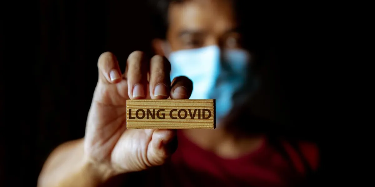 masked asian man show wooden sign with wording long covid in dark room