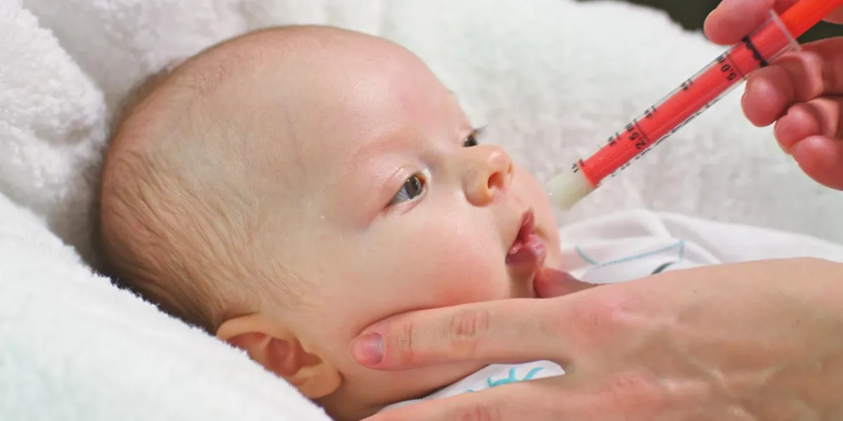 little baby girl is taking juice medicine helping by a syringe handled by mother