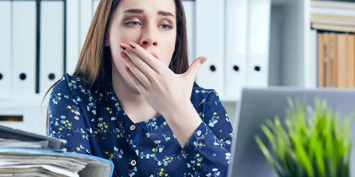 young business woman yawning at a modern office desk in front of laptop, covering her mouth chain reaction, drowsiness, unable to deal with boring job, monday after cool weekends
