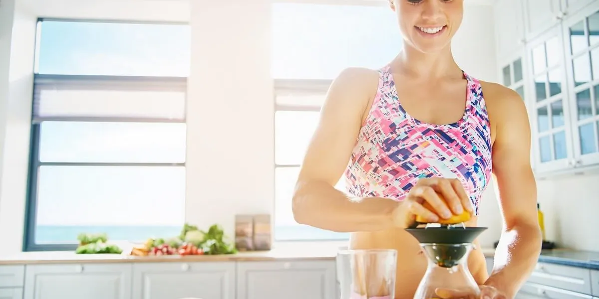happy sporty woman standing in sunlight in the kitchen making juice horizontal indoors shot