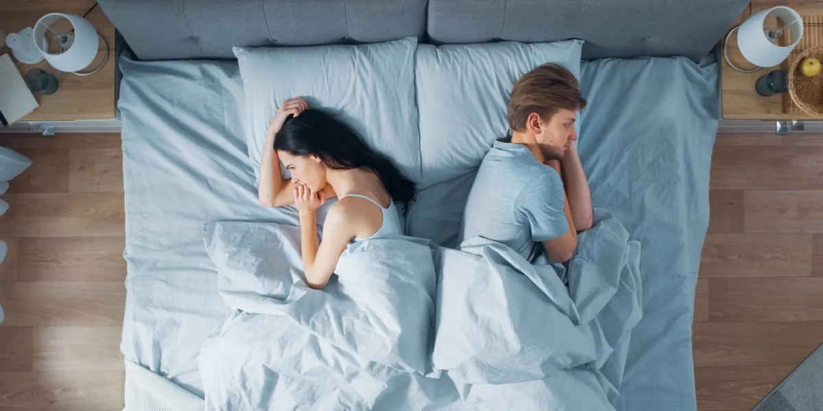 quarrelling young couple in the bed, young people lying turned away from each other and lay on their sides holding grudges and being offended