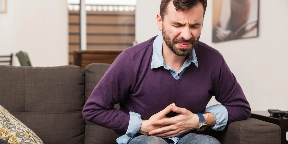 mec avec une barbe se sentant mal avec une douleur à l'estomac assis dans un canapé à la maison