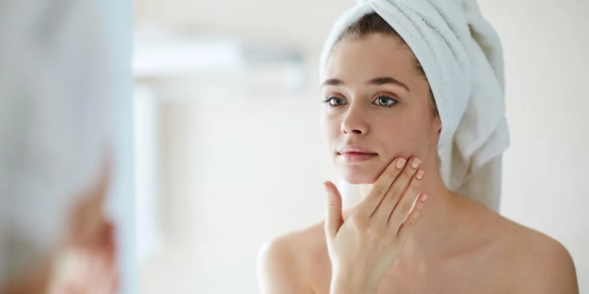 jeune femme regardant miroir dans la salle de bain et dorloter son visage