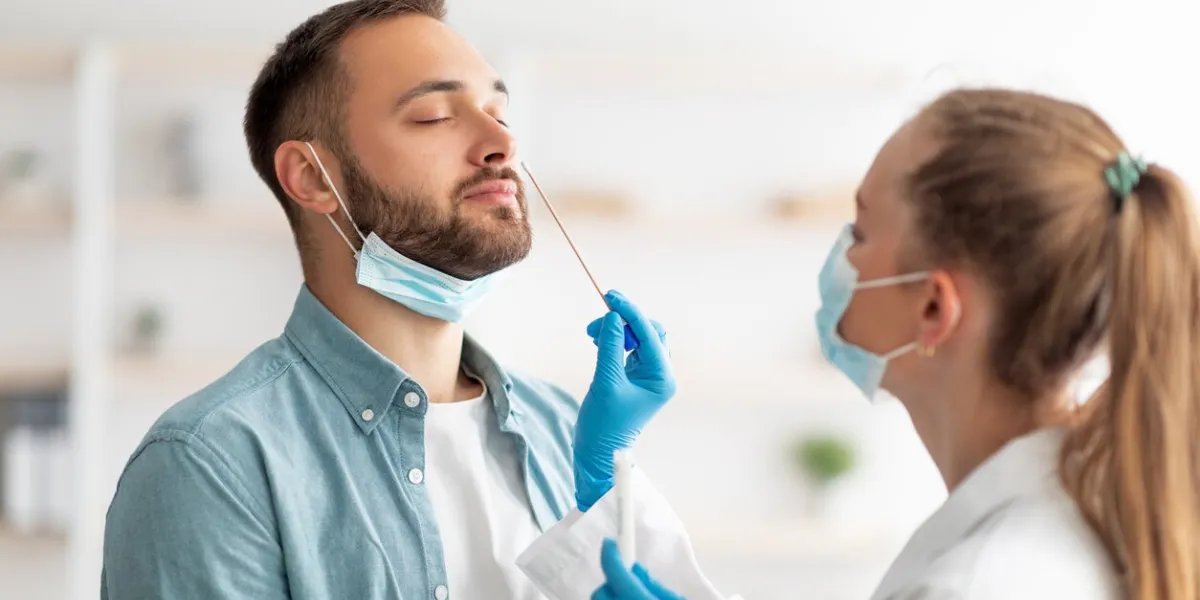 female doctor making nasal coronavirus pcr test for millennial guy at clinic young caucasian man making covid diagnostic procedure infectious disease protection concept
