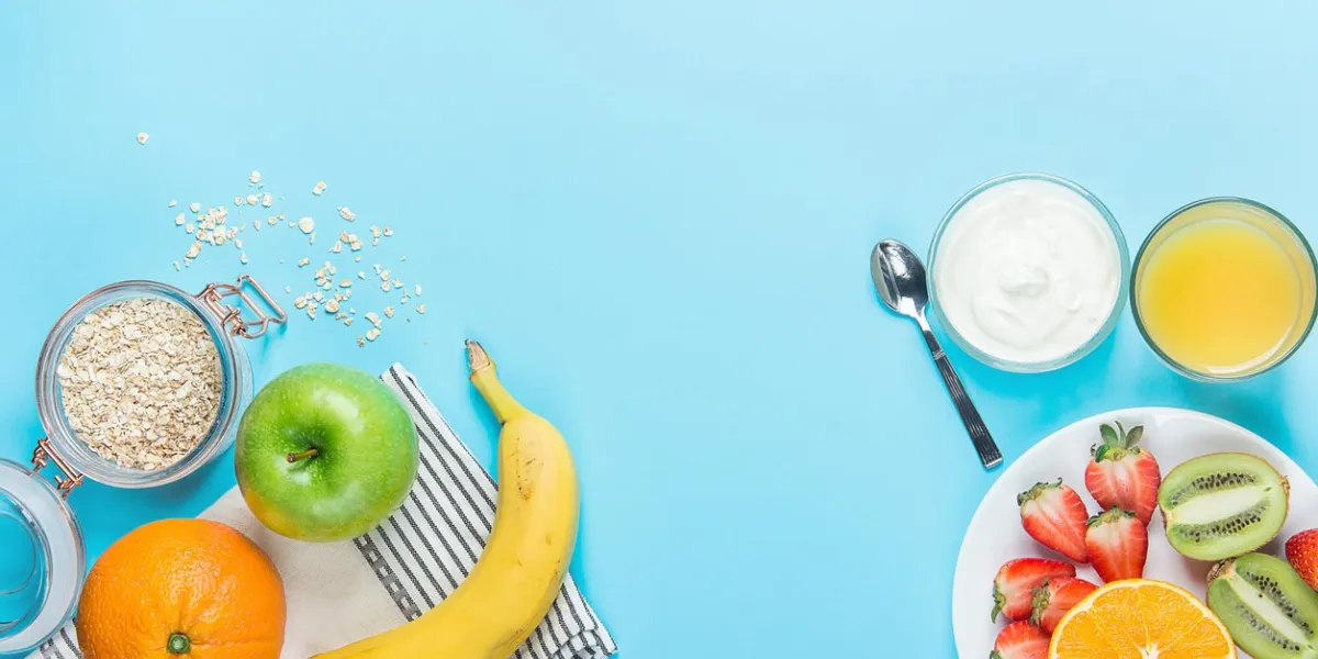 healthy breakfast ingredients oatmeal apples banana strawberries kiwi oranges yogurt juice spoon on blue table top blank mockup copy space for text flat lay composition meal planning concept