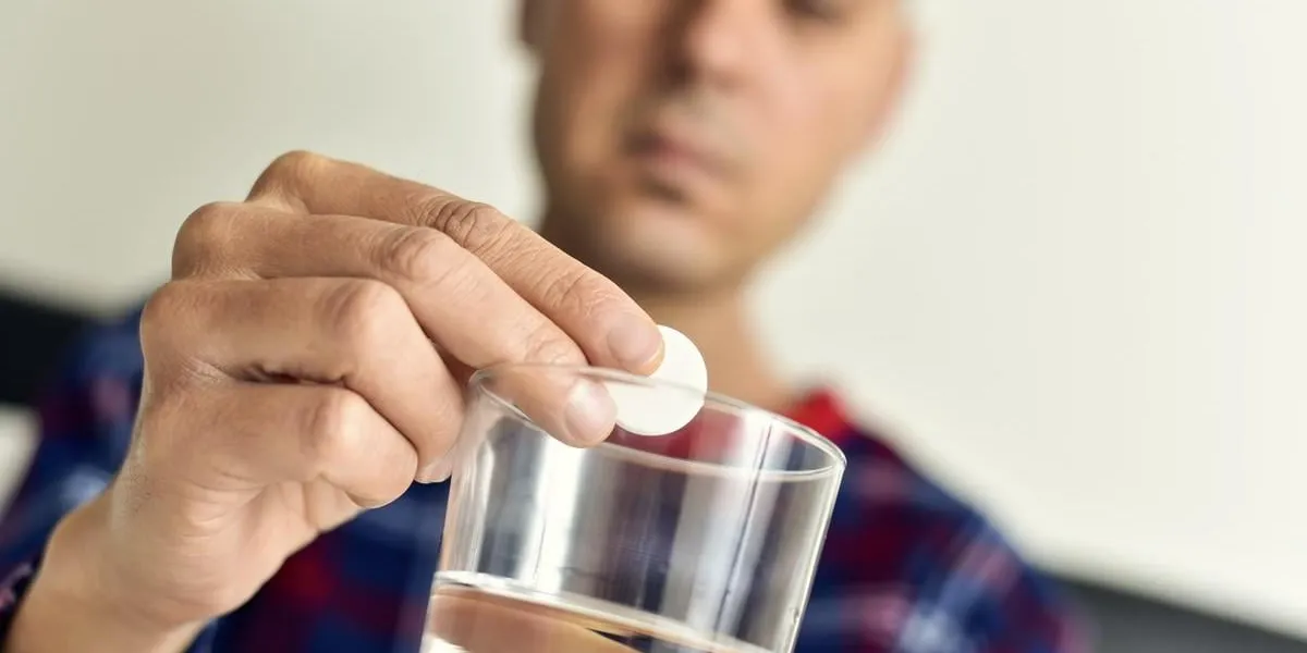 closeup of a young caucasian man in pajamas in bed about to put an effervescent tablet into a glass with water