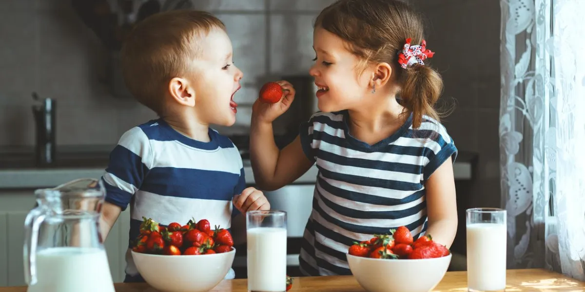 happy children girl and boy brother and sister eating strawberries with milk