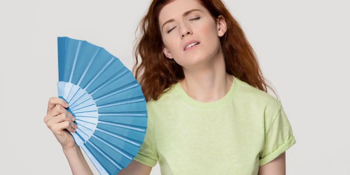 overheated redhead woman sweating feel uncomfortable suffer from heat stroke perspiration problem, tired sweaty lady waving fan cooling in hot summer weather isolated on white grey studio background