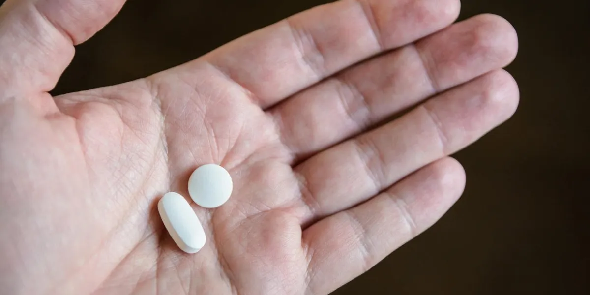close-up view of a white male hand holding two white pills in the palm against a dark background