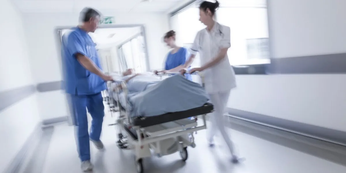 a motion blurred photograph of a senior female patient on stretcher or gurney being pushed at speed through a hospital corridor by doctors & nurses to an emergency room
