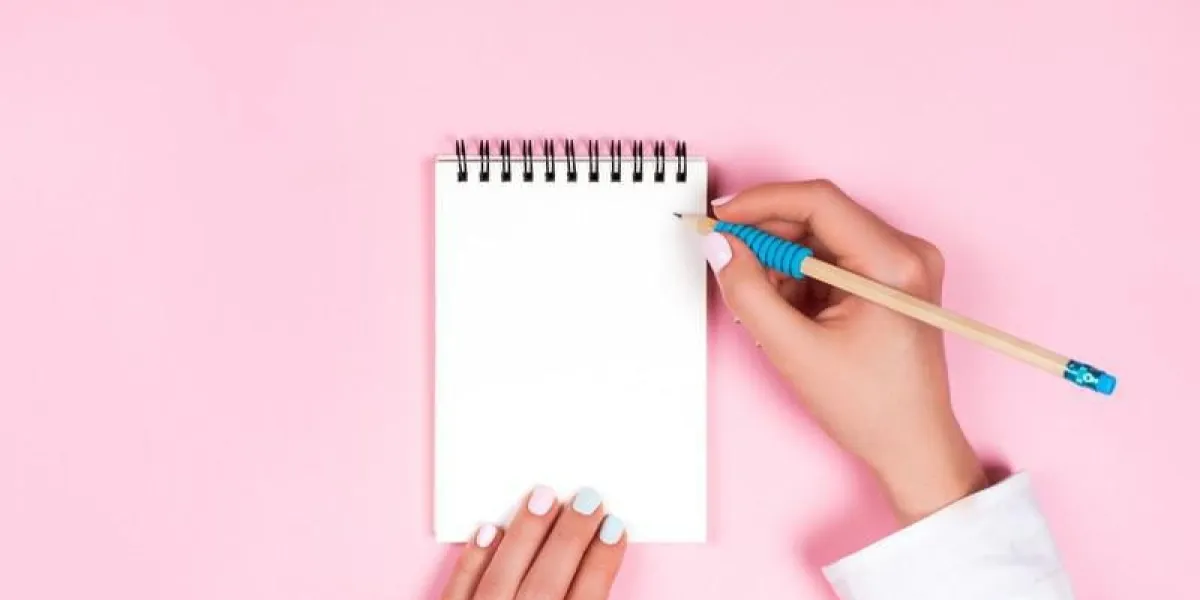 mains de la femme avec manucure parfaite tenant le crayon et le bloc-notes en spirale comme maquette pour votre fond rose design, style plat