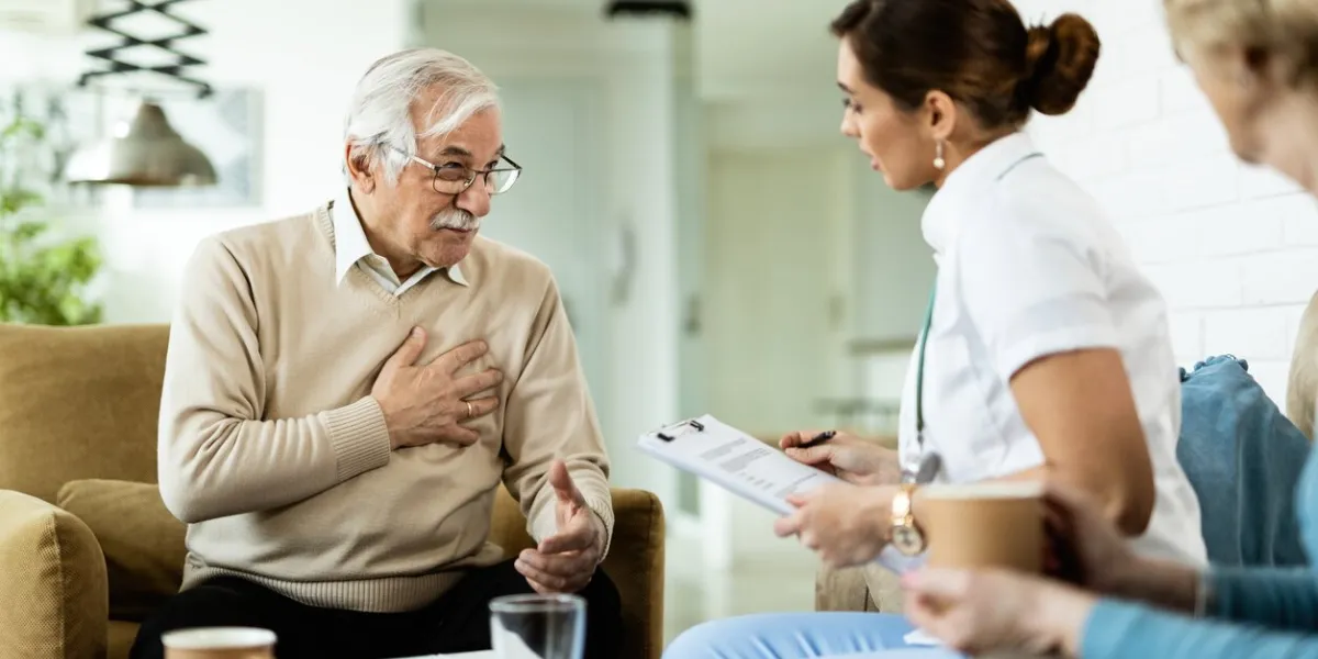 mature man communicating with female doctor and complaining of chest pain during home visit