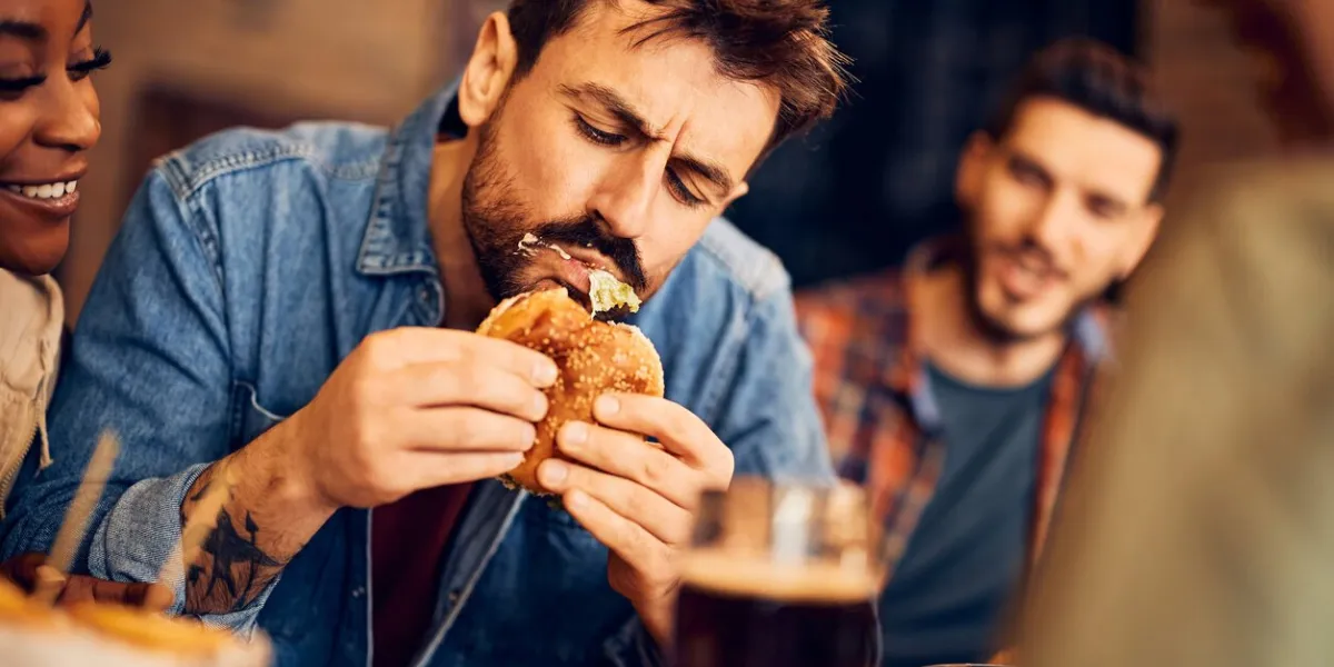 hungry man eating burger while gathering with friends in a pub