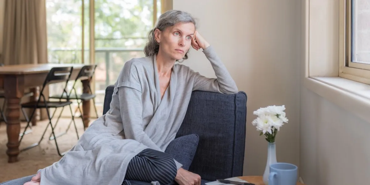 middle aged woman sitting on chair in living room looking out window (selective focus)