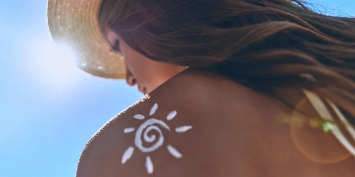 low angle rear view of young woman with a suntan lotion on her shoulder sunbathing while sitting outdoors