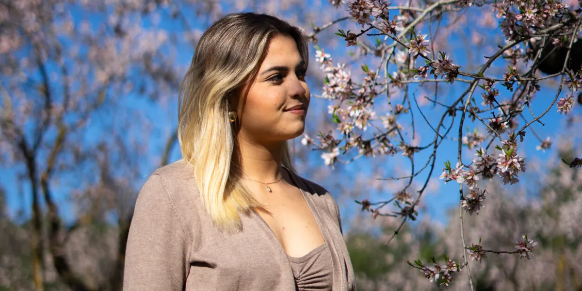 blonde woman looking at almond blossoms in an orchard during spring