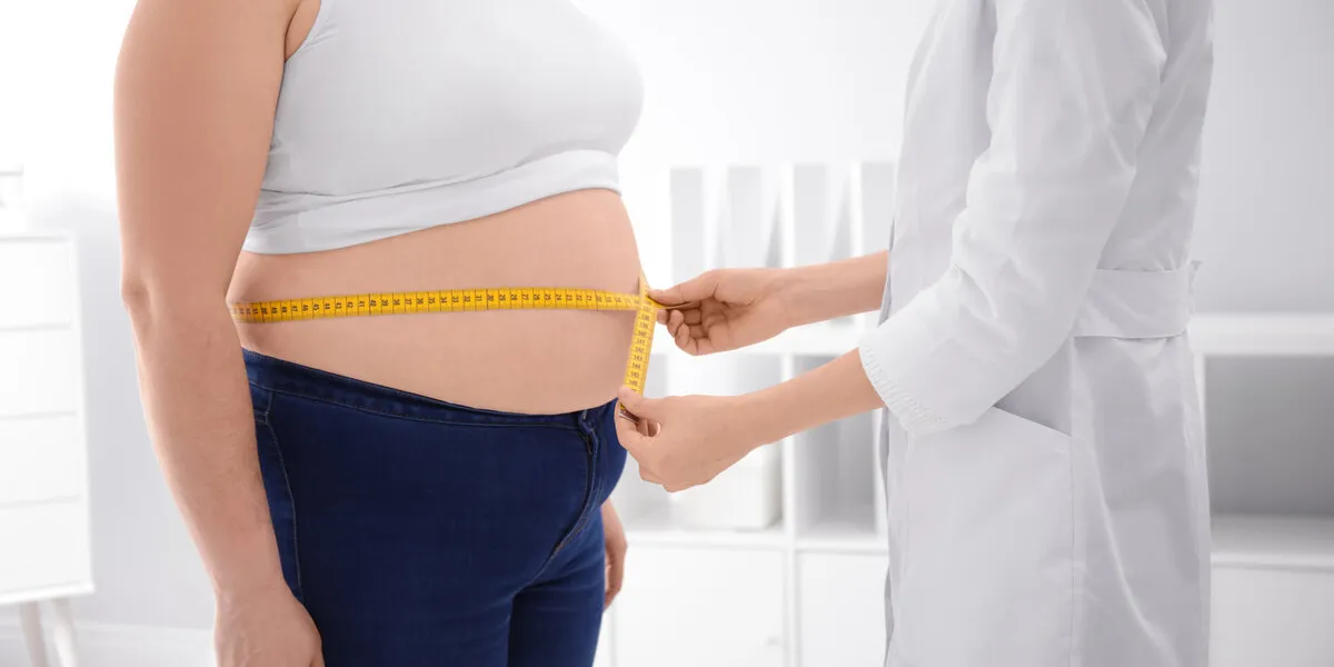 doctor measuring waist of overweight woman in clinic, closeup