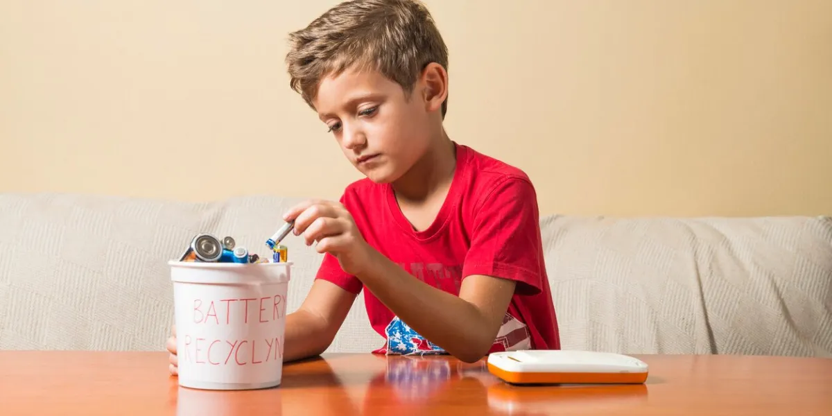 a child removing a flat battery from a toy and placing it in a recycling bin concept of educating children in environmental values