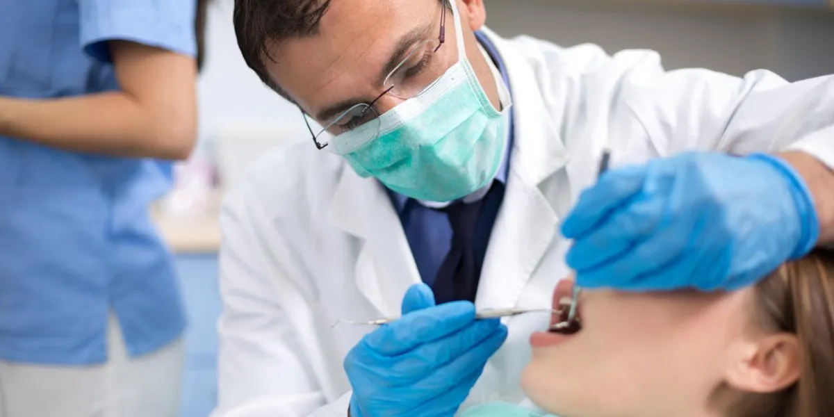 dentist with protective mask and gloves repair tooth of his young female client at ambulant