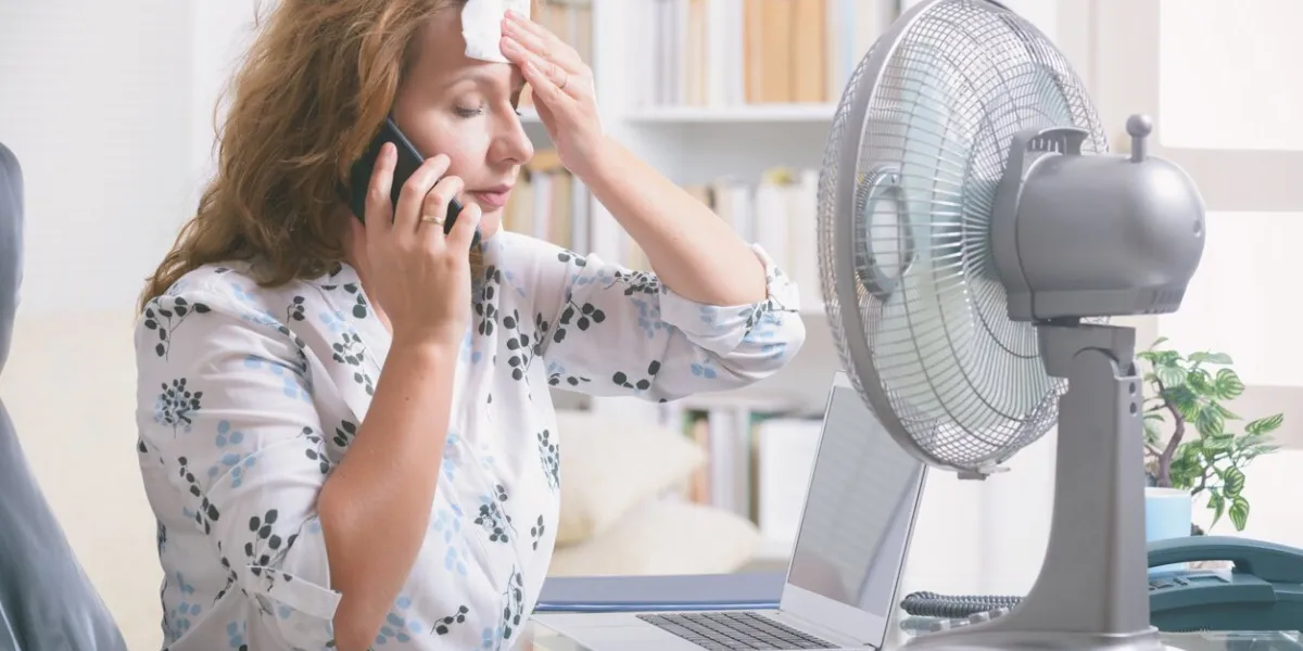 woman suffers from heat while working in the office and tries to cool off by the fan