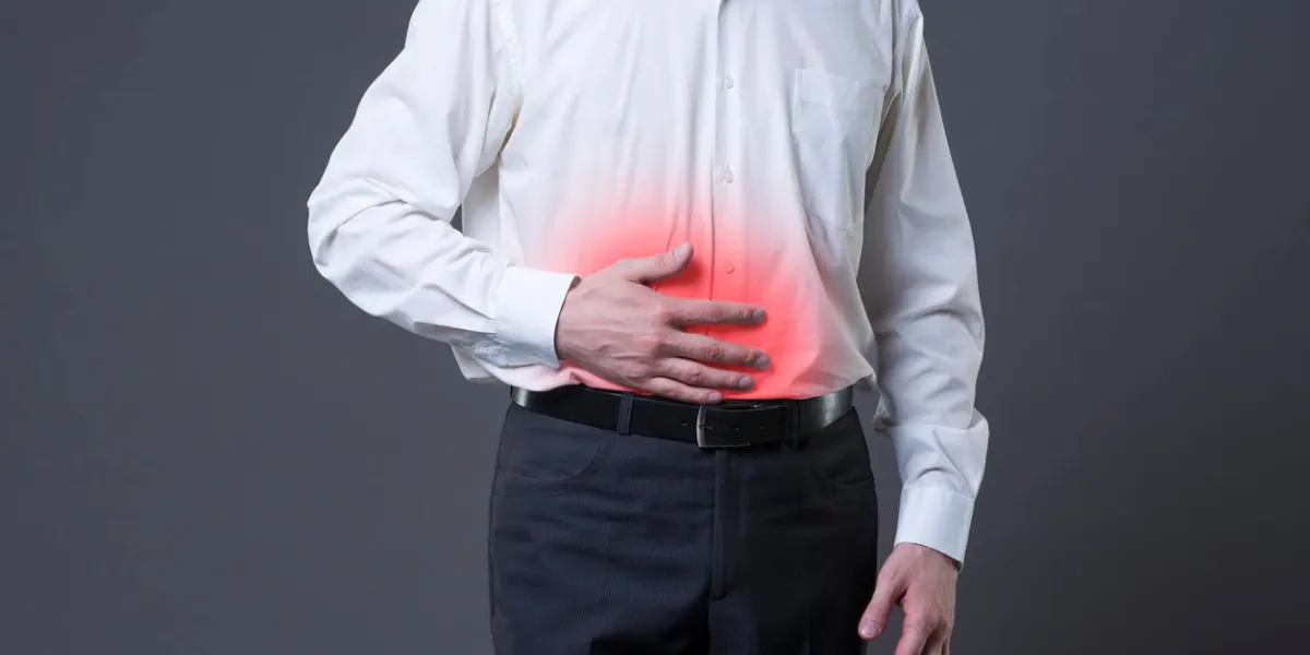homme avec des douleurs abdominales, mal de ventre sur fond gris, studio tourné avec des taches rouges